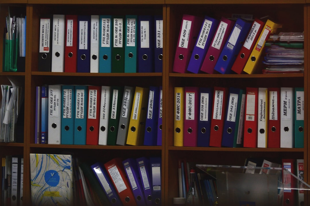 Rows of colorful ring binders organized on wooden shelves in an office