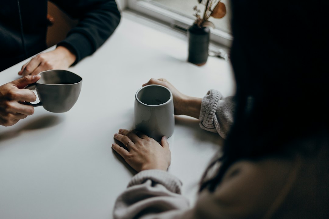 two people holding gray mugs at table
