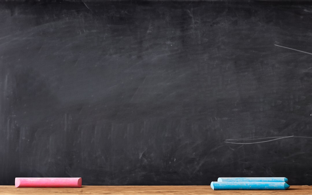 A pink chalk stick and two blue chalk sticks on a wooden ledge