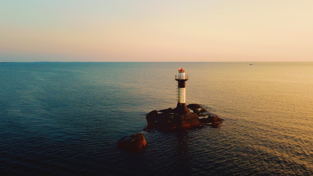 white and red lighthouse on rock formation near body of water during daytime