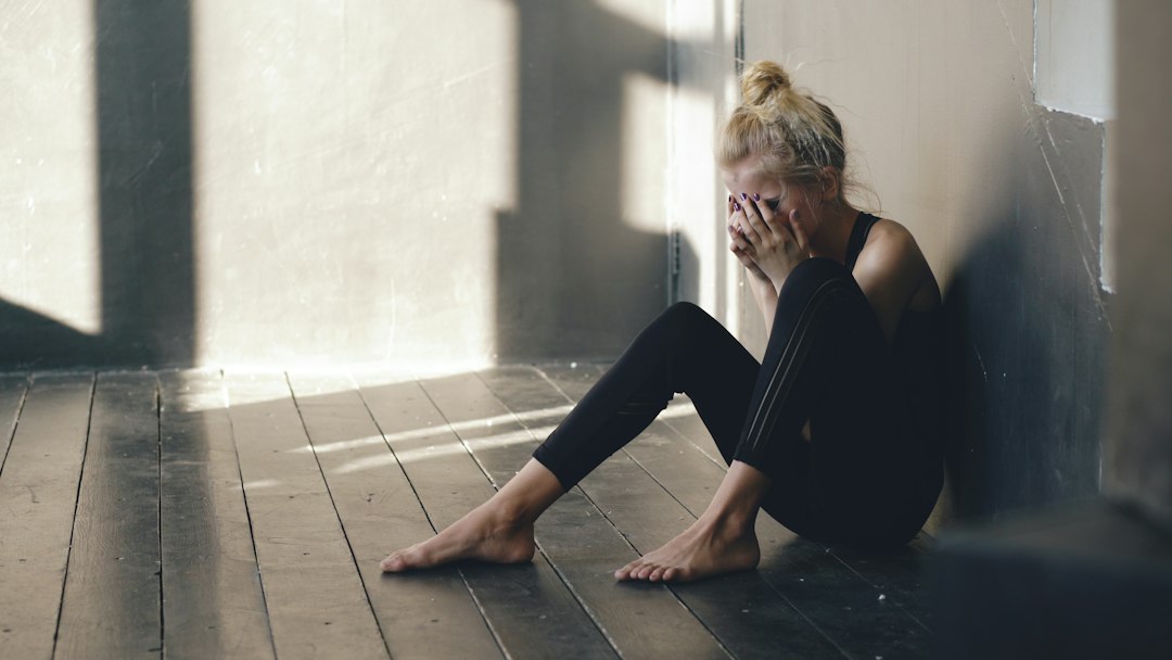 Woman sitting on floor, covering face with hands